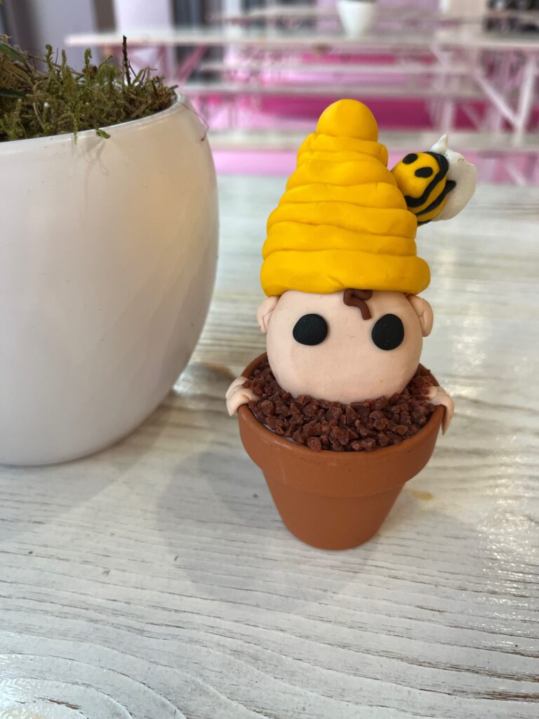 Een poppetje met een bijenhoed in een potje, gemaakt van polymeerklei.